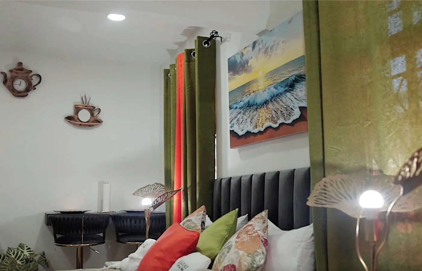 The Airbnb bedroom with green velvet curtains, a grey headboard, and a seascape painting